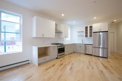 This is an example of a medium sized classic l-shaped kitchen in New York with shaker cabinets, grey cabinets, white splashback, metro tiled splashback, stainless steel appliances, light hardwood flooring, no island and brown floors.