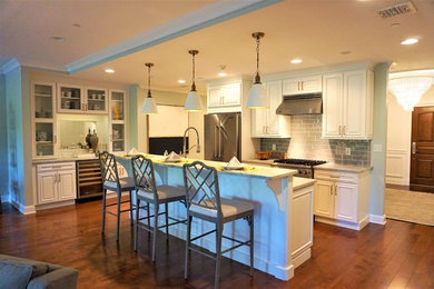 Example of a mid-sized transitional galley medium tone wood floor and brown floor open concept kitchen design in New York with an undermount sink, raised-panel cabinets, white cabinets, granite countertops, gray backsplash, glass tile backsplash, stainless steel appliances, an island and gray countertops