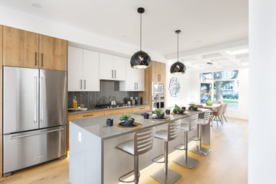 Inspiration for a contemporary galley medium tone wood floor and brown floor kitchen remodel in Calgary with an undermount sink, flat-panel cabinets, white cabinets, black backsplash, stainless steel appliances, an island and gray countertops