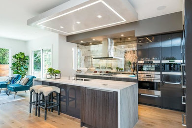 This is an example of a medium sized modern l-shaped kitchen in San Francisco with a submerged sink, flat-panel cabinets, marble worktops, medium hardwood flooring, an island, brown floors, black cabinets, metallic splashback, mirror splashback and stainless steel appliances.