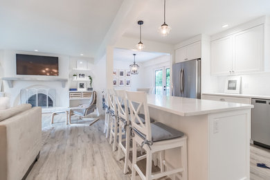 Example of a mid-sized arts and crafts u-shaped laminate floor and beige floor open concept kitchen design in Vancouver with a farmhouse sink, shaker cabinets, white cabinets, quartz countertops, white backsplash, ceramic backsplash, stainless steel appliances, an island and white countertops