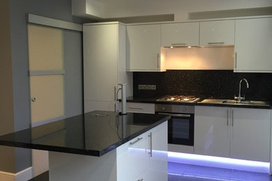 This is an example of a medium sized contemporary single-wall open plan kitchen in London with a double-bowl sink, flat-panel cabinets, white cabinets, laminate countertops, black splashback, stainless steel appliances, ceramic flooring and an island.
