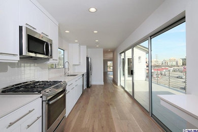 Photo of a large contemporary single-wall enclosed kitchen in Los Angeles with a double-bowl sink, white cabinets, engineered stone countertops, white splashback, stainless steel appliances, light hardwood flooring and no island.