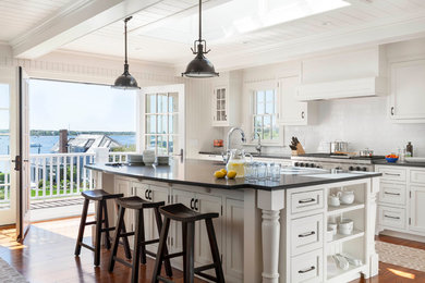 Large beach style galley medium tone wood floor and brown floor kitchen photo in Boston with shaker cabinets, white cabinets, white backsplash, subway tile backsplash, stainless steel appliances, an island, an undermount sink and solid surface countertops