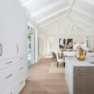 Photo of an expansive tropical galley open plan kitchen in Miami with a double-bowl sink, recessed-panel cabinets, grey cabinets, wood benchtops, stainless steel appliances, light hardwood floors, with island, beige floor and white benchtop.