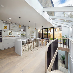 Idee per una cucina contemporanea di medie dimensioni con lavello sottopiano, ante con bugna sagomata, ante grigie, paraspruzzi a specchio, elettrodomestici da incasso, parquet chiaro, pavimento beige e top bianco