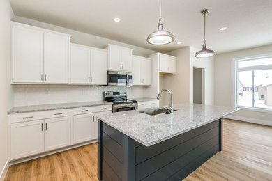 Example of a mid-sized cottage galley light wood floor and beige floor open concept kitchen design in Cedar Rapids with an undermount sink, shaker cabinets, white cabinets, granite countertops, white backsplash, ceramic backsplash, stainless steel appliances, an island and gray countertops