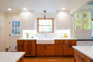 Example of a mid-sized farmhouse u-shaped medium tone wood floor and brown floor kitchen design in Columbus with a farmhouse sink, recessed-panel cabinets, medium tone wood cabinets, quartzite countertops, white backsplash, stone slab backsplash, an island and white countertops