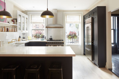 Example of a classic u-shaped light wood floor kitchen design in New York with a farmhouse sink, recessed-panel cabinets, white backsplash, subway tile backsplash and a peninsula
