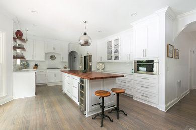 Example of a mid-sized minimalist l-shaped medium tone wood floor and brown floor open concept kitchen design in Charleston with an undermount sink, shaker cabinets, white cabinets, white backsplash, subway tile backsplash, stainless steel appliances, an island and white countertops