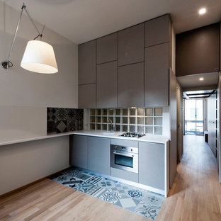 This is an example of a small modern single-wall eat-in kitchen in Milan with an integrated sink, flat-panel cabinets, grey cabinets, solid surface benchtops, white splashback, glass sheet splashback, stainless steel appliances and ceramic floors.