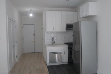 Example of a minimalist porcelain tile and gray floor kitchen design in New York with white cabinets, white backsplash, subway tile backsplash, stainless steel appliances and white countertops