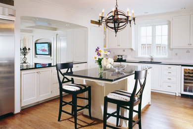 Klassisk inredning av ett mellanstort u-kök, med en undermonterad diskho, luckor med profilerade fronter, vita skåp, vitt stänkskydd, stänkskydd i keramik, rostfria vitvaror, mellanmörkt trägolv, en köksö och brunt golv