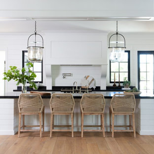 Country single-wall kitchen in Phoenix with shaker cabinets, white cabinets, soapstone benchtops, with island, black benchtop, white splashback, timber splashback, medium hardwood floors and brown floor.