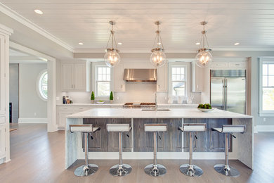Example of a large beach style u-shaped light wood floor and brown floor open concept kitchen design in Other with an undermount sink, recessed-panel cabinets, white cabinets, marble countertops, gray backsplash, subway tile backsplash, stainless steel appliances and an island