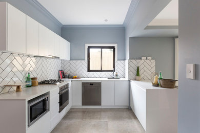 Modern inredning av ett avskilt l-kök, med släta luckor, vita skåp, vitt stänkskydd, rostfria vitvaror, en halv köksö och grått golv