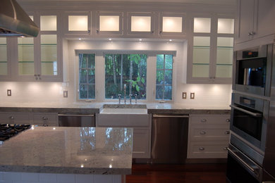 Kitchen - large traditional medium tone wood floor kitchen idea in Miami with a farmhouse sink, shaker cabinets, white cabinets, white backsplash, subway tile backsplash, stainless steel appliances and an island