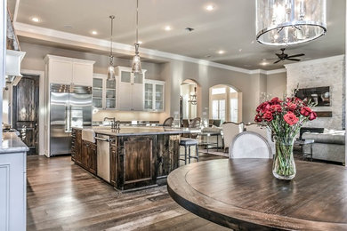 Example of a mid-sized cottage chic l-shaped dark wood floor and brown floor open concept kitchen design in Houston with a farmhouse sink, shaker cabinets, white cabinets, white backsplash, stainless steel appliances and an island