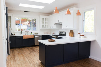 Example of a large transitional u-shaped medium tone wood floor and brown floor kitchen design in San Francisco with a farmhouse sink, stainless steel appliances, white backsplash, subway tile backsplash, white countertops, shaker cabinets, white cabinets and a peninsula