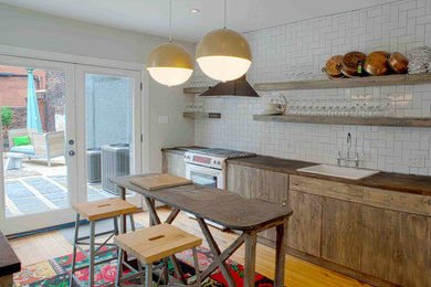 Inspiration for a mid-sized eclectic light wood floor enclosed kitchen remodel in Philadelphia with a single-bowl sink, flat-panel cabinets, medium tone wood cabinets, wood countertops, white backsplash, subway tile backsplash, white appliances and an island