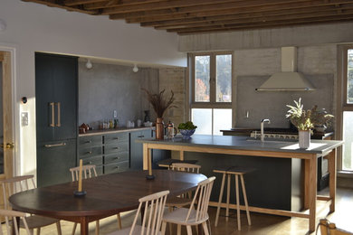 Example of a minimalist l-shaped light wood floor eat-in kitchen design in New York with a single-bowl sink, flat-panel cabinets, green cabinets, wood countertops, paneled appliances and an island