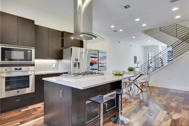 Mid-sized trendy l-shaped dark wood floor and brown floor open concept kitchen photo in Austin with an undermount sink, flat-panel cabinets, dark wood cabinets, quartzite countertops, beige backsplash, ceramic backsplash, stainless steel appliances and an island