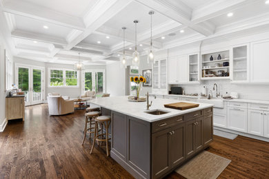 Inspiration for a large traditional galley kitchen/diner in New York with a belfast sink, shaker cabinets, white cabinets, white splashback, ceramic splashback, stainless steel appliances, medium hardwood flooring, an island and brown floors.