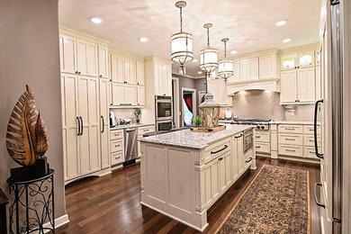 Large elegant u-shaped dark wood floor and brown floor enclosed kitchen photo in Nashville with recessed-panel cabinets, white cabinets, granite countertops, beige backsplash, ceramic backsplash, stainless steel appliances, an island, multicolored countertops and a farmhouse sink