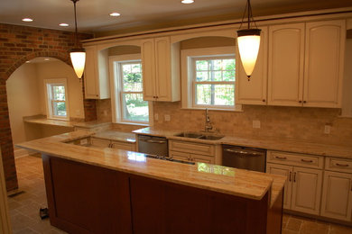 Example of a huge classic travertine floor enclosed kitchen design in Cleveland with an undermount sink, raised-panel cabinets, granite countertops, beige backsplash, stone tile backsplash, stainless steel appliances and an island