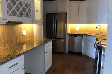 Example of a mid-sized trendy u-shaped medium tone wood floor and brown floor enclosed kitchen design in Chicago with shaker cabinets, white cabinets, granite countertops, brown countertops, an undermount sink, beige backsplash, glass sheet backsplash and stainless steel appliances