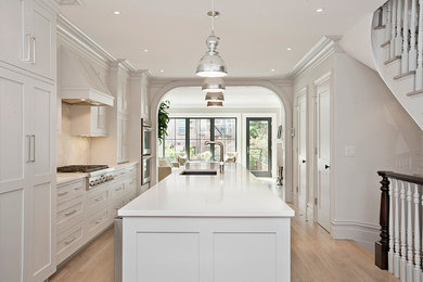 Inspiration for a large transitional single-wall light wood floor eat-in kitchen remodel in New York with an undermount sink, shaker cabinets, gray cabinets, quartz countertops, white backsplash, stone slab backsplash, stainless steel appliances and an island
