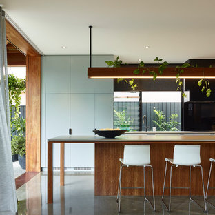 Photo of a contemporary galley kitchen in Brisbane with an undermount sink, flat-panel cabinets, medium wood cabinets, black splashback, concrete floors, with island, grey floor and grey benchtop.