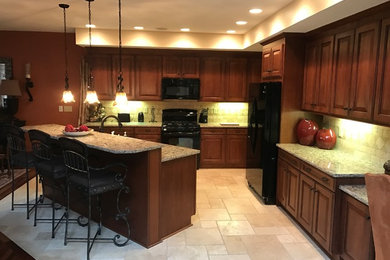 Large arts and crafts l-shaped travertine floor and beige floor open concept kitchen photo in Other with raised-panel cabinets, medium tone wood cabinets, granite countertops, beige backsplash, stone tile backsplash, black appliances and an island