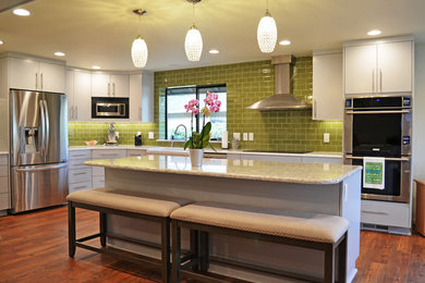 Eat-in kitchen - large contemporary l-shaped medium tone wood floor and multicolored floor eat-in kitchen idea in Portland with a farmhouse sink, flat-panel cabinets, gray cabinets, quartzite countertops, green backsplash, glass tile backsplash, stainless steel appliances, an island and gray countertops