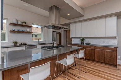 Example of a large trendy l-shaped light wood floor open concept kitchen design in Denver with an undermount sink, flat-panel cabinets, white cabinets, stainless steel countertops, white backsplash, glass tile backsplash, stainless steel appliances and an island