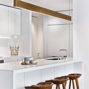 Ispirazione per una cucina ad U minimalista con lavello sottopiano, ante lisce, ante bianche, parquet chiaro, isola, pavimento beige e top bianco