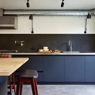 Industrial Küche mit integriertem Waschbecken, flächenbündigen Schrankfronten, schwarzen Schränken, Edelstahl-Arbeitsplatte, Küchenrückwand in Schwarz, Küchengeräten aus Edelstahl, Betonboden, Kücheninsel, grauem Boden und grauer Arbeitsplatte in London
