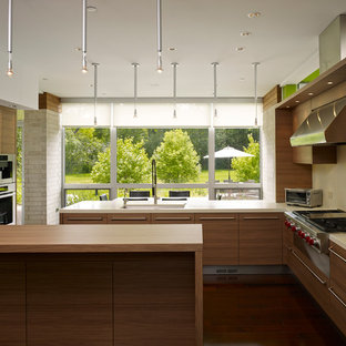 Idée de décoration pour une grand cuisine américaine design en U avec un évier encastré, des portes de placard en bois brun, une crédence beige, un électroménager en acier inoxydable, un îlot central, un placard à porte plane, un sol en vinyl et un sol marron.