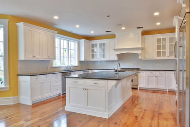 Example of a mid-sized classic u-shaped medium tone wood floor and brown floor enclosed kitchen design in New York with an undermount sink, white backsplash, glass tile backsplash, shaker cabinets, stainless steel appliances and an island
