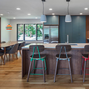 Immagine di una cucina abitabile minimalista di medie dimensioni con lavello sottopiano, ante lisce, ante blu, top in quarzo composito, paraspruzzi bianco, paraspruzzi con piastrelle in ceramica, elettrodomestici in acciaio inossidabile, parquet chiaro e penisola