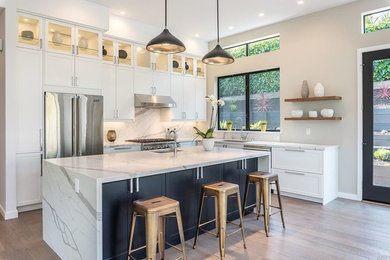 Inspiration for a large contemporary u-shaped medium tone wood floor open concept kitchen remodel in San Francisco with a drop-in sink, shaker cabinets, white cabinets, marble countertops, white backsplash, marble backsplash, stainless steel appliances and an island