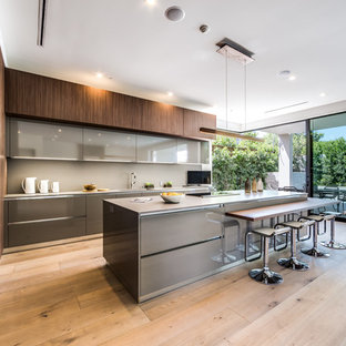 This is an example of a large modern open plan kitchen in Los Angeles with brown cabinets, granite benchtops, grey splashback, light hardwood floors, with island, flat-panel cabinets and stainless steel appliances.