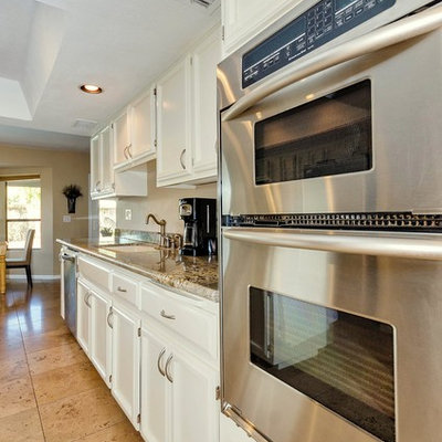 Example of a mid-sized tuscan galley travertine floor eat-in kitchen design in Phoenix with an undermount sink, recessed-panel cabinets, white cabinets, granite countertops, stainless steel appliances and an island