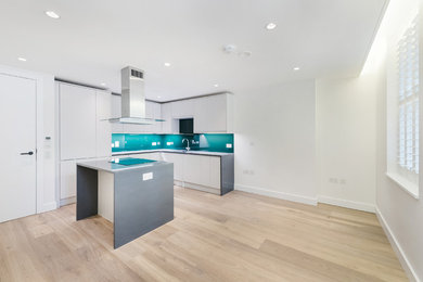 Photo of a contemporary kitchen in London with white cabinets, granite worktops, green splashback, glass sheet splashback, laminate floors and grey worktops.
