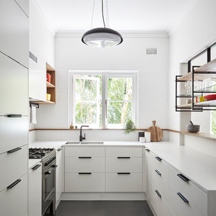Small contemporary u-shaped kitchen in Sydney with an undermount sink, flat-panel cabinets, white cabinets, quartz benchtops, white splashback, ceramic splashback, concrete floors, a peninsula, grey floor and panelled appliances.