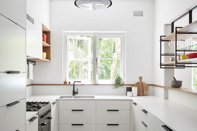 Small contemporary u-shaped kitchen in Sydney with a submerged sink, flat-panel cabinets, white cabinets, engineered stone countertops, white splashback, ceramic splashback, concrete flooring, a breakfast bar, grey floors and integrated appliances.