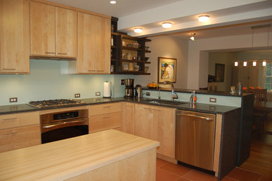 This is an example of a medium sized contemporary l-shaped kitchen/diner in DC Metro with a submerged sink, flat-panel cabinets, light wood cabinets, granite worktops, white splashback, glass tiled splashback, stainless steel appliances, terracotta flooring, a breakfast bar, red floors and black worktops.