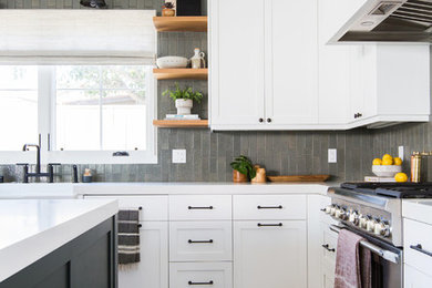 Mid-sized transitional l-shaped light wood floor and beige floor kitchen photo in San Diego with a farmhouse sink, shaker cabinets, white cabinets, solid surface countertops, gray backsplash, subway tile backsplash, paneled appliances and an island