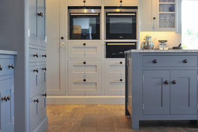 ハンプシャーにある高級な広いコンテンポラリースタイルのおしゃれなキッチン (ドロップインシンク、青いキャビネット、御影石カウンター、黒い調理設備、セラミックタイルの床) の写真