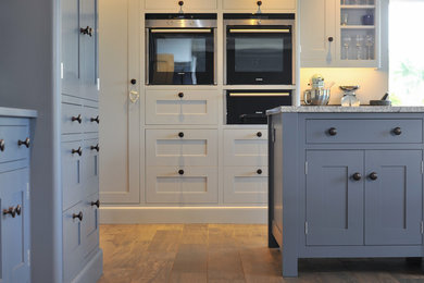 This is an example of a large contemporary open plan kitchen in Hampshire with a built-in sink, blue cabinets, granite worktops, black appliances, ceramic flooring and an island.